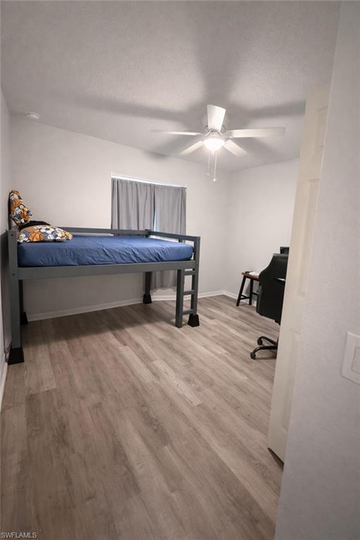 Bedroom featuring light wood-style floors, a ceiling fan, an office area, and a textured ceiling