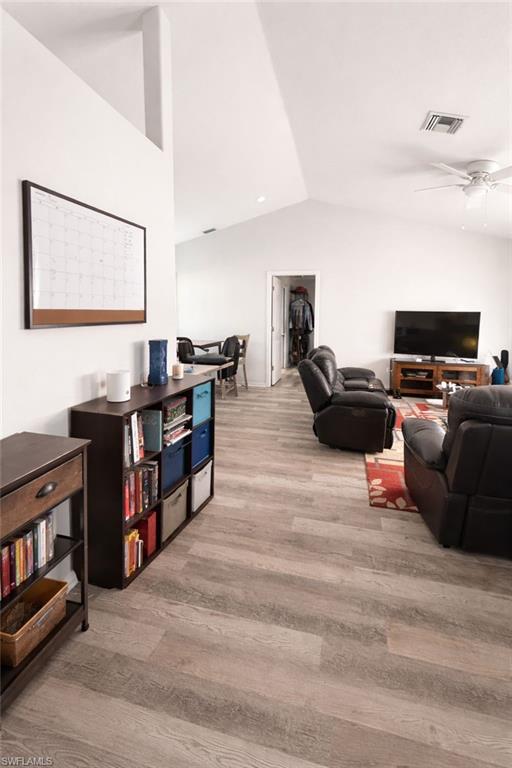 Living room featuring lofted ceiling, ceiling fan, and light wood-type flooring