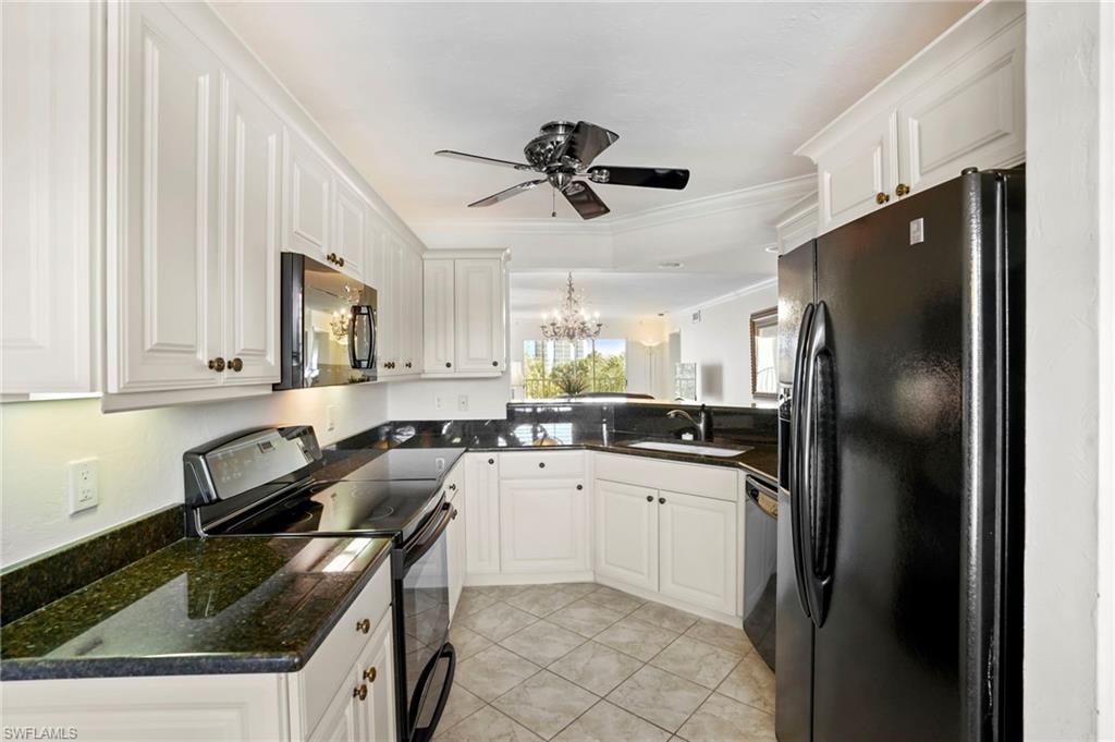 Kitchen with black appliances, a chandelier, white cabinetry, ornamental molding, and dark stone countertops