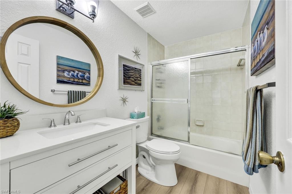 Bathroom with vanity, light wood finished floors, enclosed tub / shower combo, and a textured ceiling
