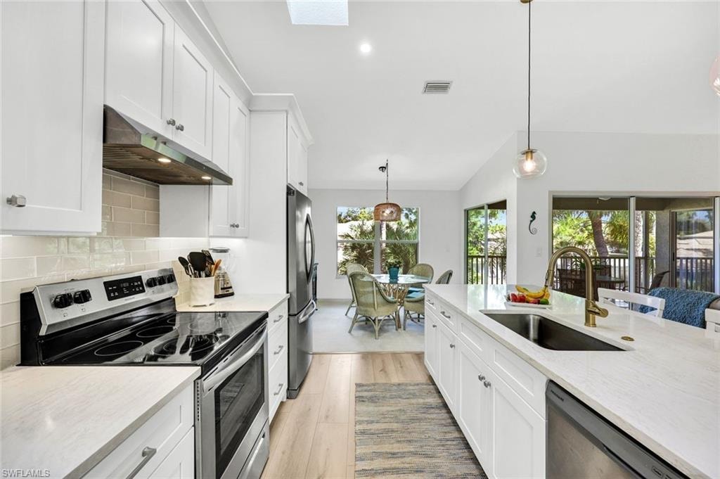 Kitchen featuring stainless steel appliances, white cabinets, pendant lighting, and lofted ceiling