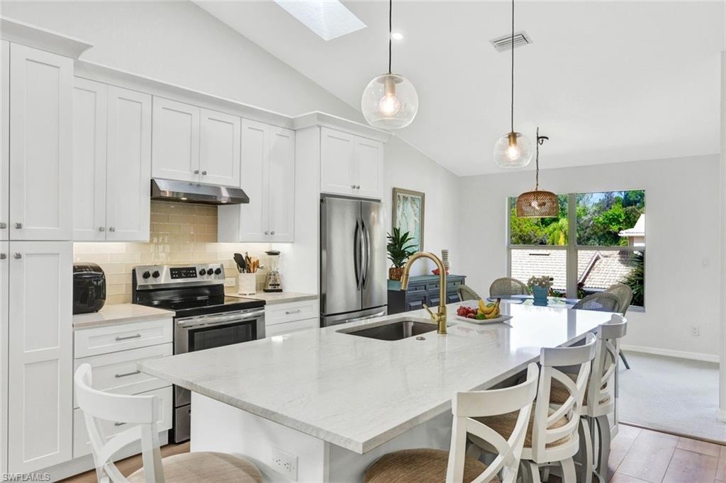 Kitchen with lofted ceiling, stainless steel appliances, light stone counters, a kitchen bar, and a skylight