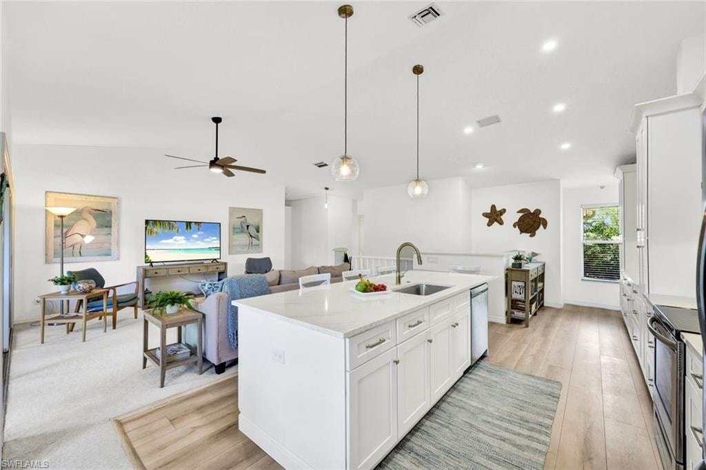 Kitchen featuring white cabinetry, an island with sink, pendant lighting, light stone counters, and vaulted ceiling