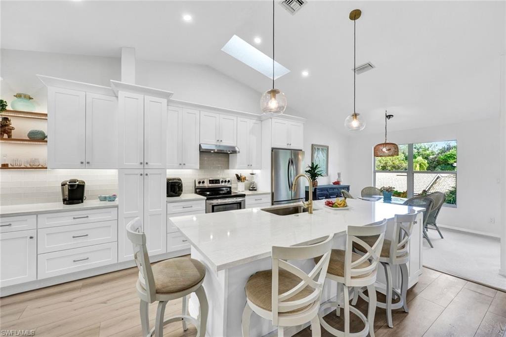 Kitchen with a breakfast bar area, a skylight, white cabinets, light stone countertops, and vaulted ceiling