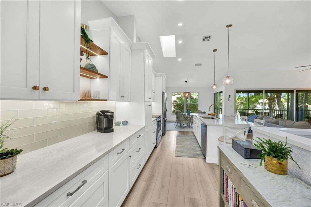 Kitchen with open shelves, white cabinetry, light stone countertops, and decorative light fixtures