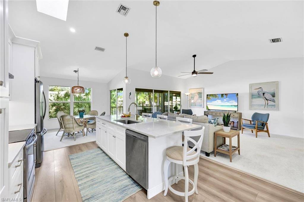 Kitchen featuring white cabinets, a breakfast bar area, stainless steel appliances, light stone counters, and pendant lighting