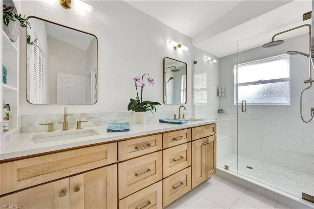 Full bath with double vanity, a shower stall, light tile patterned floors, and decorative backsplash