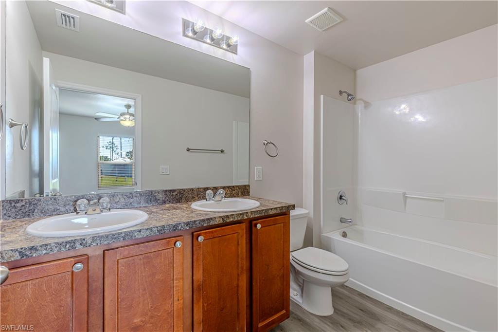 Bathroom featuring double vanity, light wood-style flooring, washtub / shower combination, and ceiling fan
