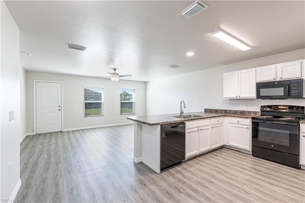 Kitchen with black appliances, dark countertops, a peninsula, white cabinetry, and light wood finished floors