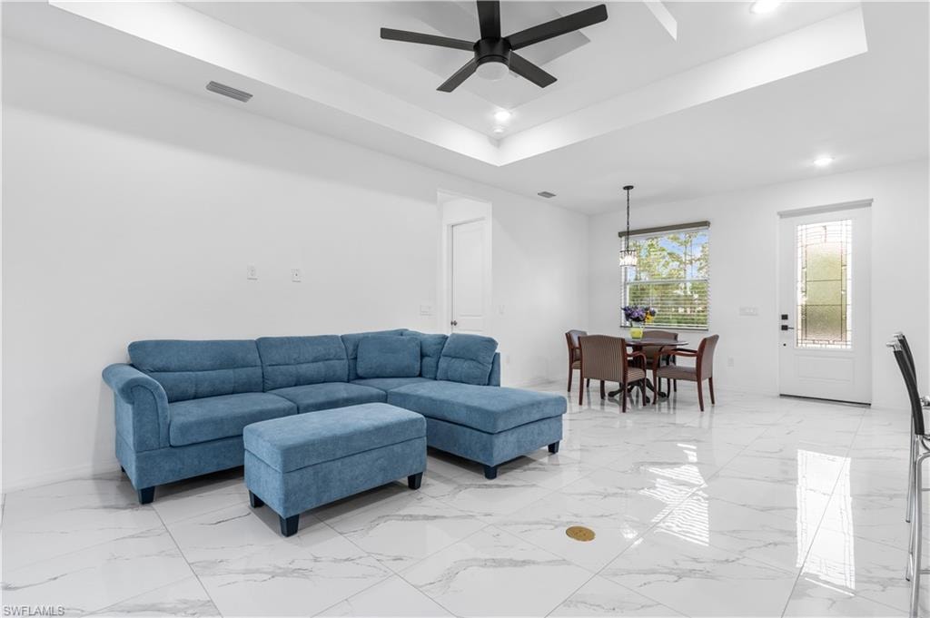 Living area with a raised ceiling, ceiling fan, recessed lighting, and light marble finish flooring