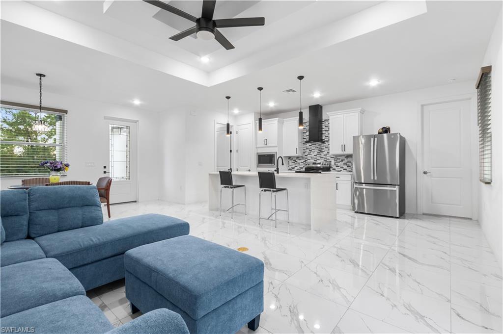Living room featuring a raised ceiling, ceiling fan, light marble finish flooring, and hanging lights