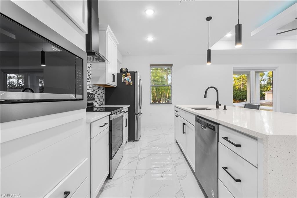 Kitchen with white cabinets, stainless steel appliances, decorative light fixtures, light stone counters, and light marble finish floors