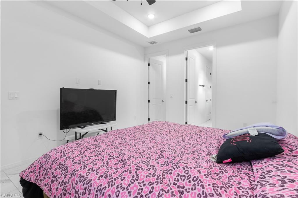 Bedroom with a raised ceiling, recessed lighting, ensuite bath, a ceiling fan, and marble look tile flooring