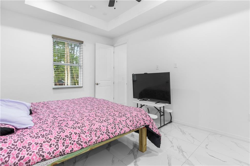 Bedroom with a raised ceiling, a ceiling fan, and marble finish floors
