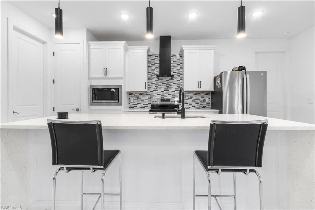 Kitchen featuring a kitchen breakfast bar, a spacious island, white cabinets, light stone counters, and stainless steel appliances