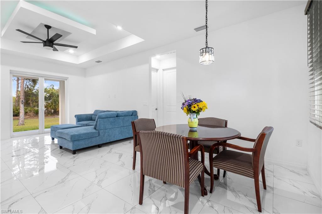 Dining area featuring light marble finish floors, a raised ceiling, and ceiling fan