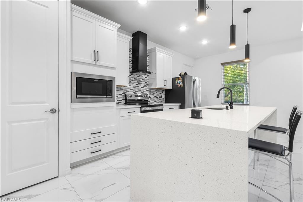 Kitchen featuring a center island with sink, decorative light fixtures, stainless steel appliances, light stone counters, and a breakfast bar area
