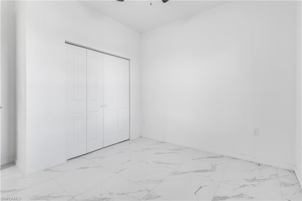Unfurnished bedroom featuring light marble finish floors, a closet, and a ceiling fan