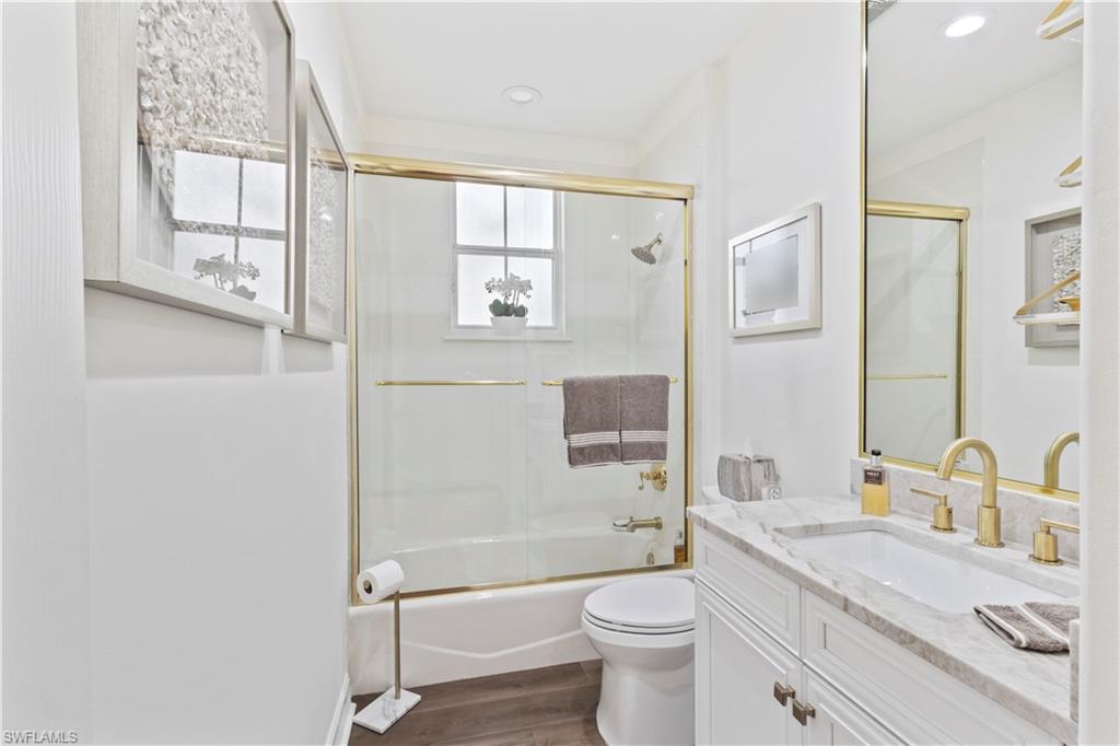 Bathroom with vanity, combined bath / shower with glass door, dark wood-type flooring, and recessed lighting