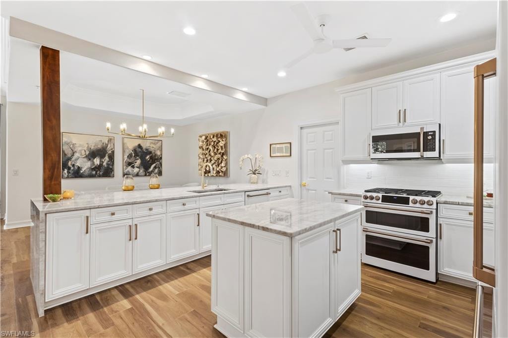 Kitchen featuring white appliances, light stone countertops, white cabinetry, a kitchen island, and a tray ceiling