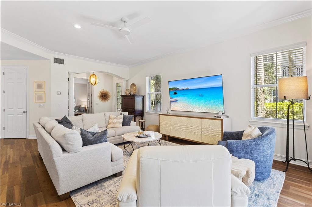 Living room featuring hardwood / wood-style floors, a ceiling fan, arched walkways, and crown molding