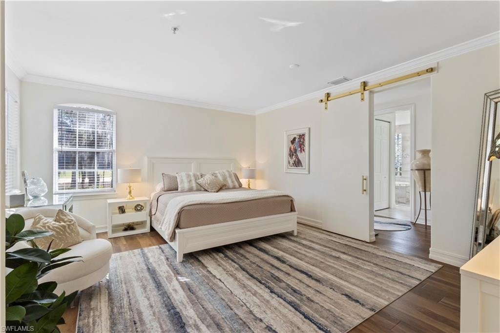 Bedroom featuring ornamental molding, a barn door, and wood finished floors