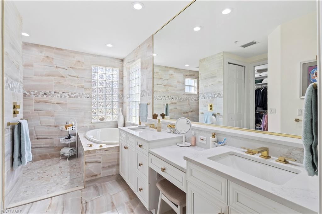 Bathroom with double vanity, a walk in shower, a bath, a walk in closet, and tile walls