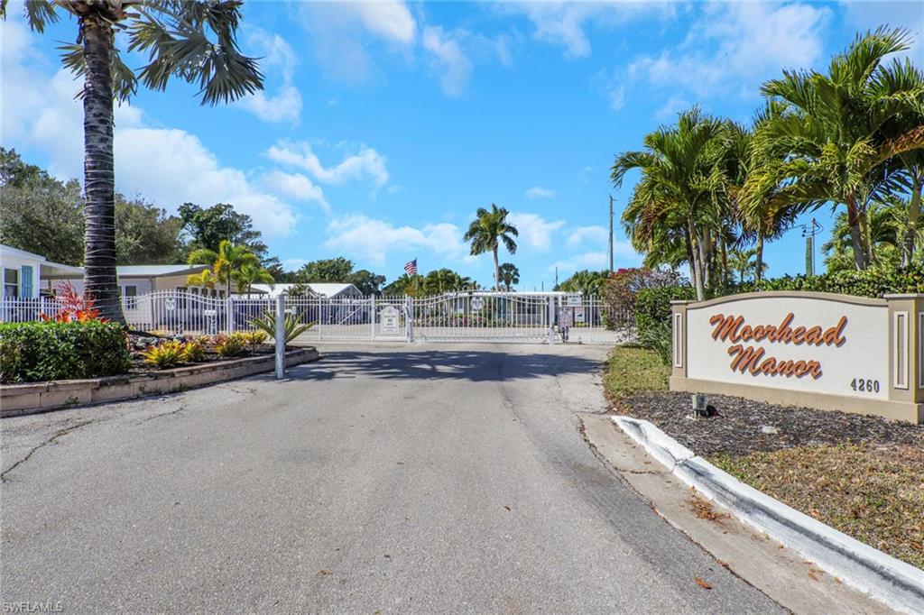 View of asphalt street with a gated entry, a gate, and curbs