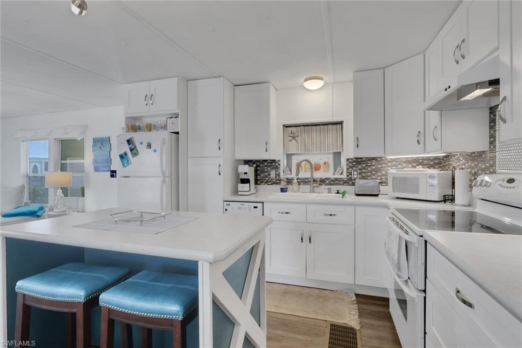 Kitchen featuring white appliances, white cabinetry, a breakfast bar, light countertops, and light wood-style flooring