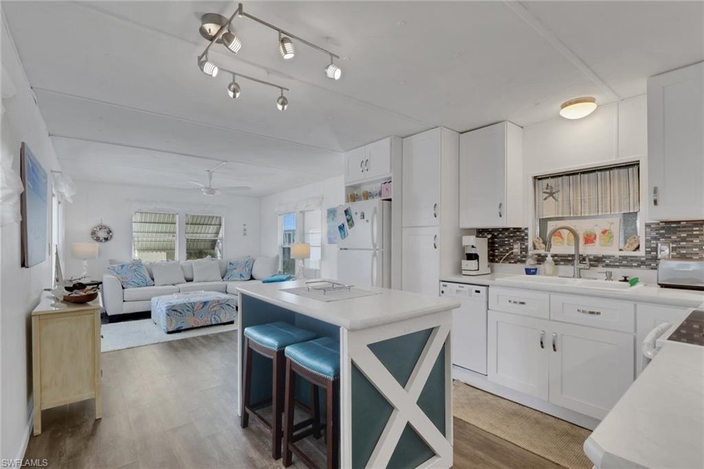 Dual tone kitchen with tasteful backsplash, a breakfast bar, white appliances, a kitchen island, and light countertops