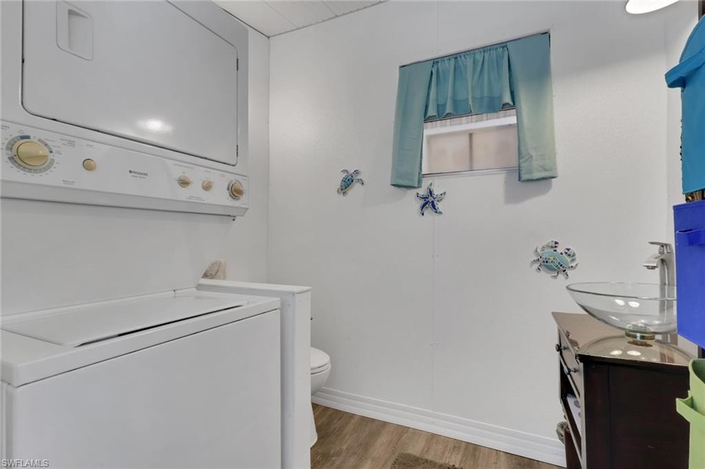 Half bathroom featuring light wood-style floors, vanity, and stacked washing machine and dryer