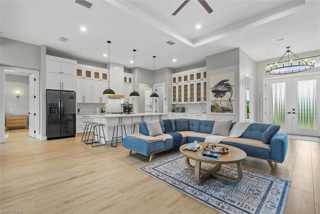 Living area featuring french doors, a ceiling fan, light wood-type flooring, a chandelier, and a tray ceiling