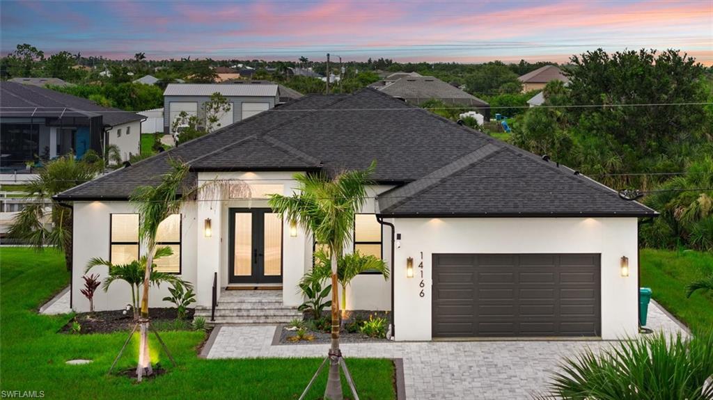View of front of property featuring french doors, stucco siding, a yard, decorative driveway, and an attached garage