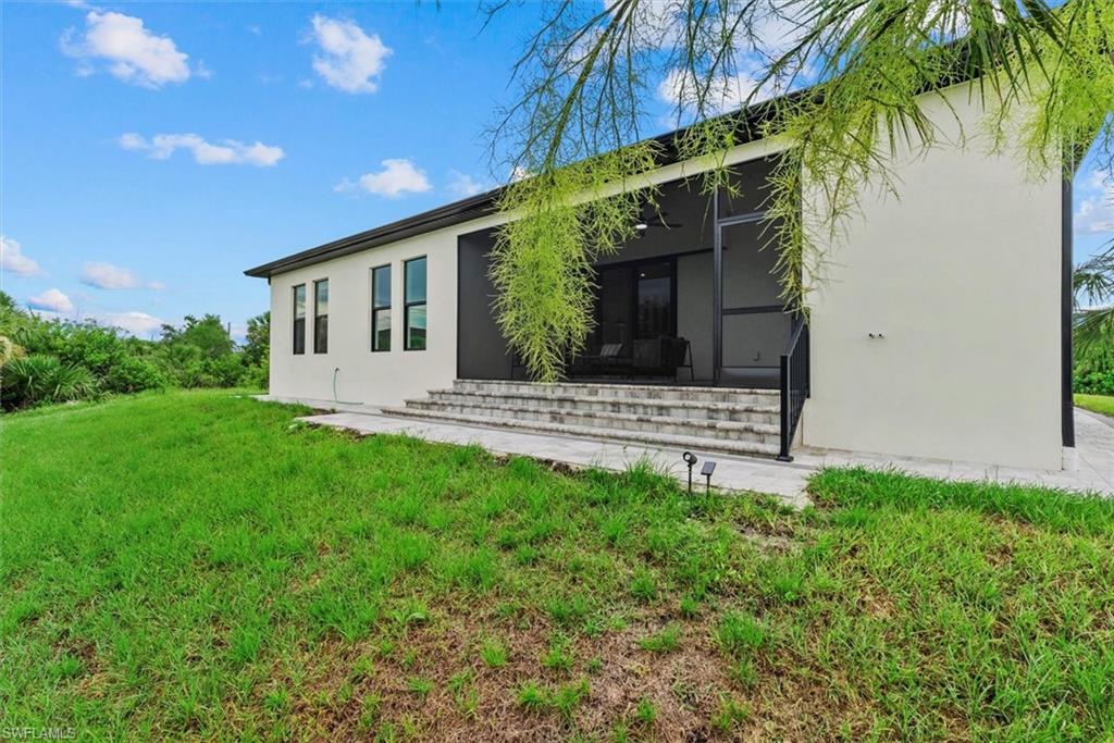 Rear view of house with stucco siding, a lawn, entry steps, and a sunroom