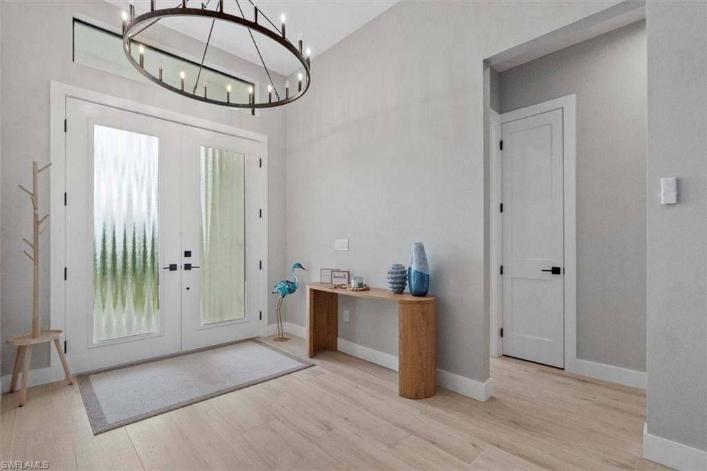 Entrance foyer with french doors, light wood-style floors, a chandelier, and a high ceiling