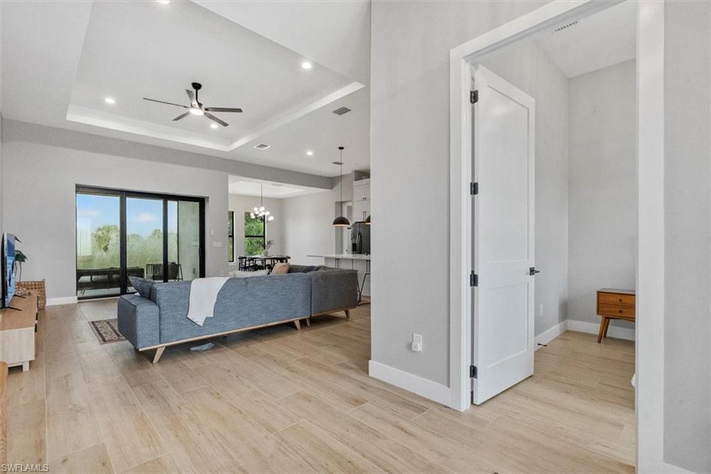 Living area with hanging lights, a ceiling fan, light wood-style flooring, and a raised ceiling
