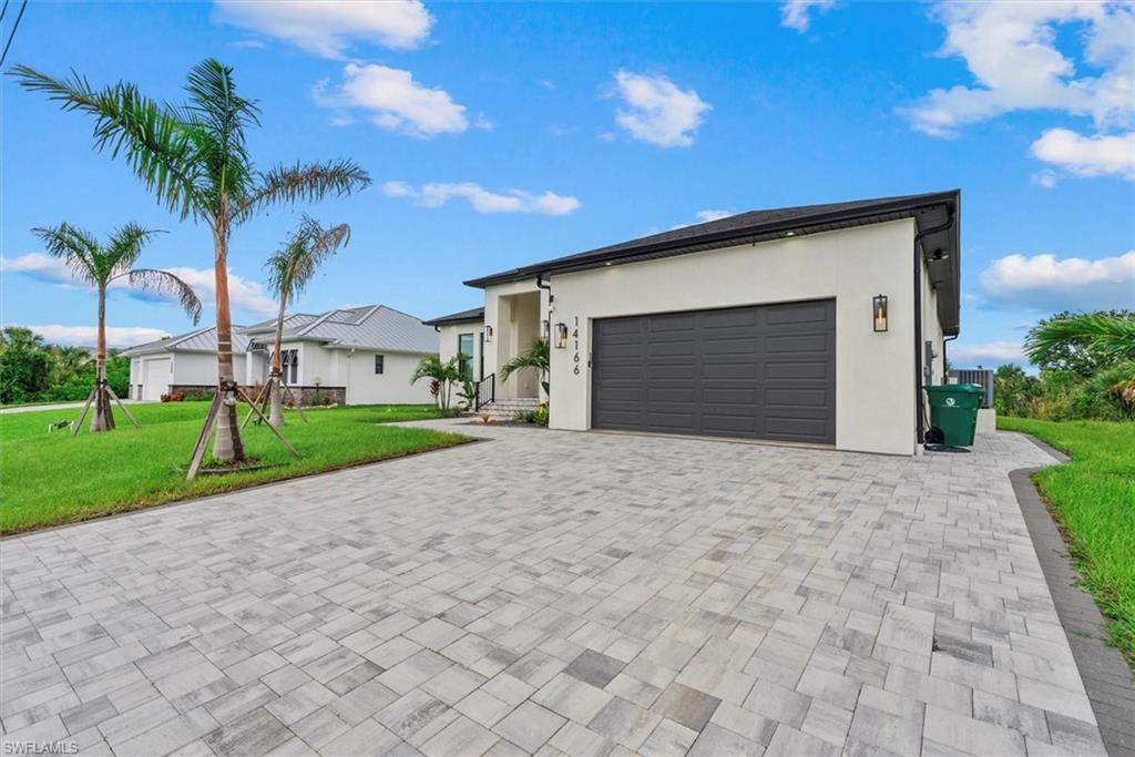 View of front of property with a front lawn, stucco siding, a garage, and decorative driveway