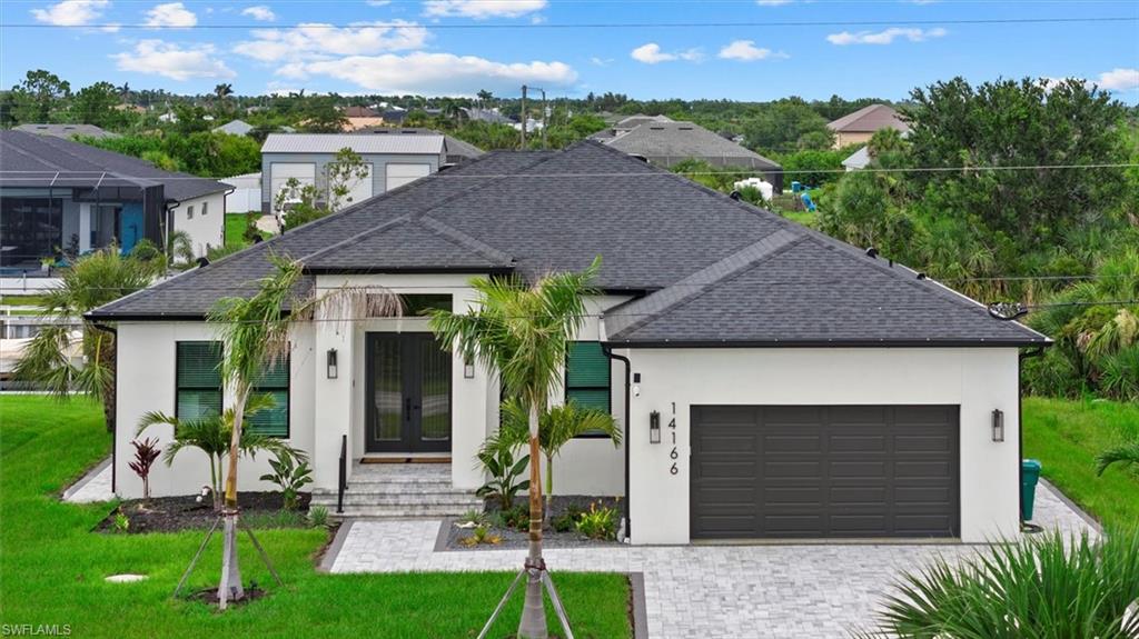 View of front of property with french doors, stucco siding, an attached garage, a front lawn, and decorative driveway