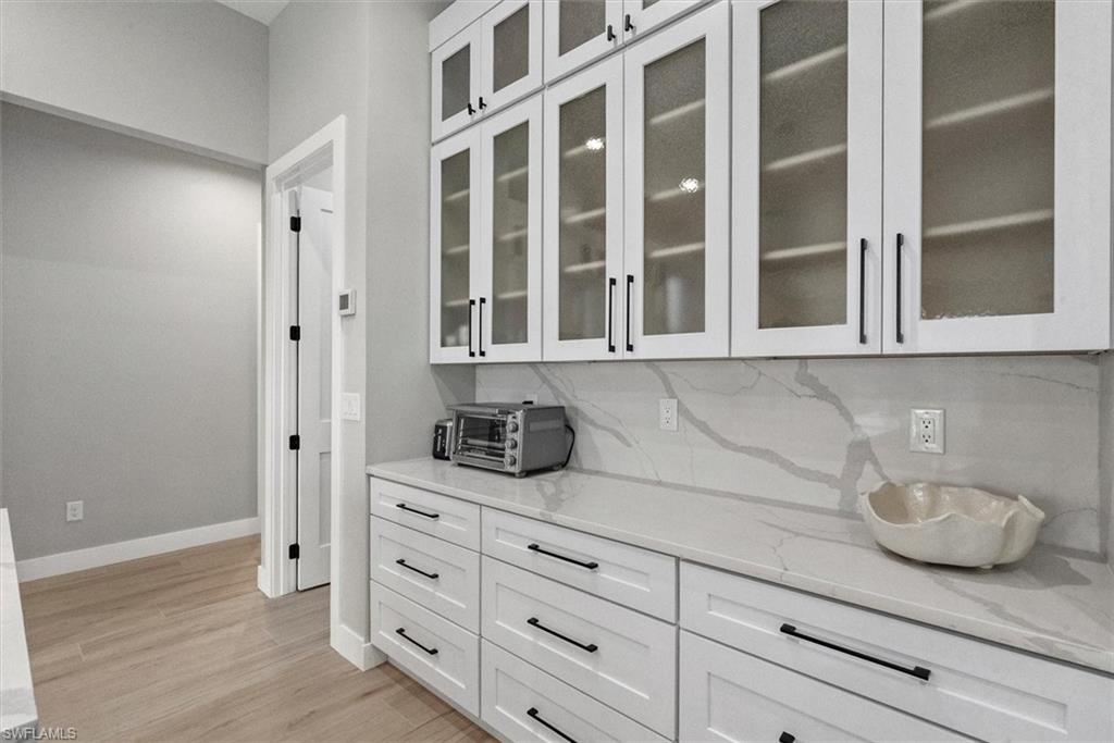 Bar with white cabinetry, light stone countertops, glass insert cabinets, and light wood-style floors