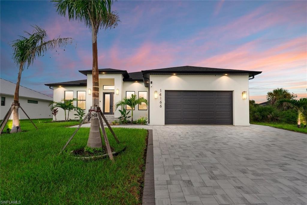 Modern home with stucco siding, an attached garage, a front yard, and decorative driveway