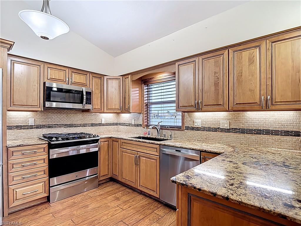 Kitchen with lofted ceiling, stainless steel appliances, light stone countertops, wood finish cabinets, and light wood-type flooring