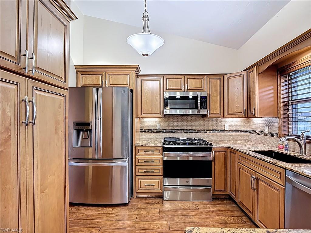 Kitchen with vaulted ceiling, stainless steel appliances, light stone countertops, hanging light fixtures, and light wood-type flooring