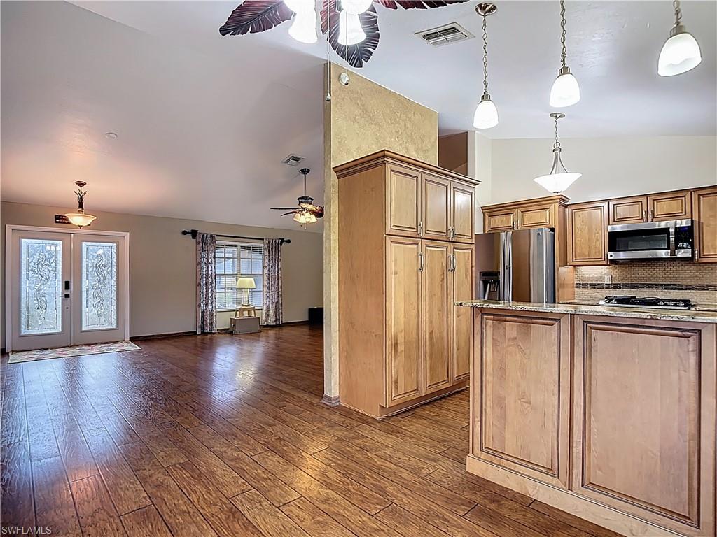 Kitchen with hanging light fixtures, stainless steel appliances, lofted ceiling, decorative backsplash, and dark wood-style floors