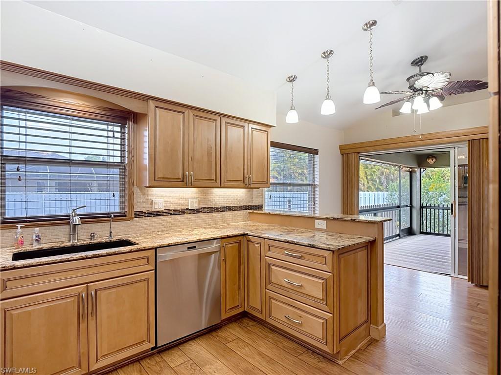 Kitchen featuring hanging light fixtures, light stone counters, dishwasher, lofted ceiling, and ceiling fan