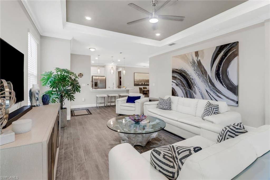 Living area featuring a ceiling fan, recessed lighting, a tray ceiling, light wood-style flooring, and ornamental molding