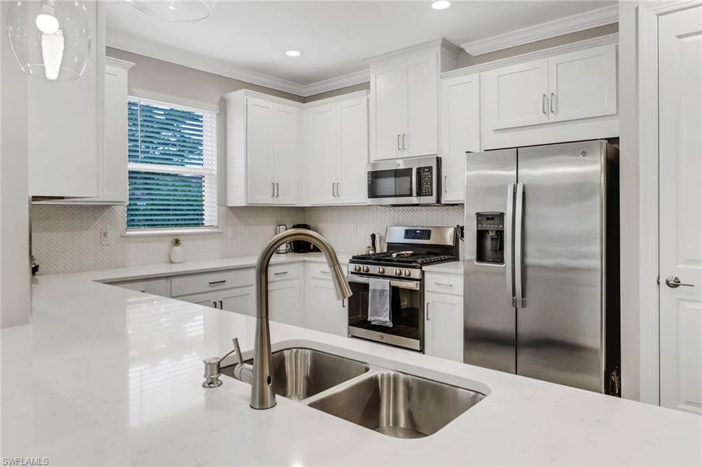 Kitchen featuring stainless steel appliances, white cabinets, light stone counters, ornamental molding, and backsplash