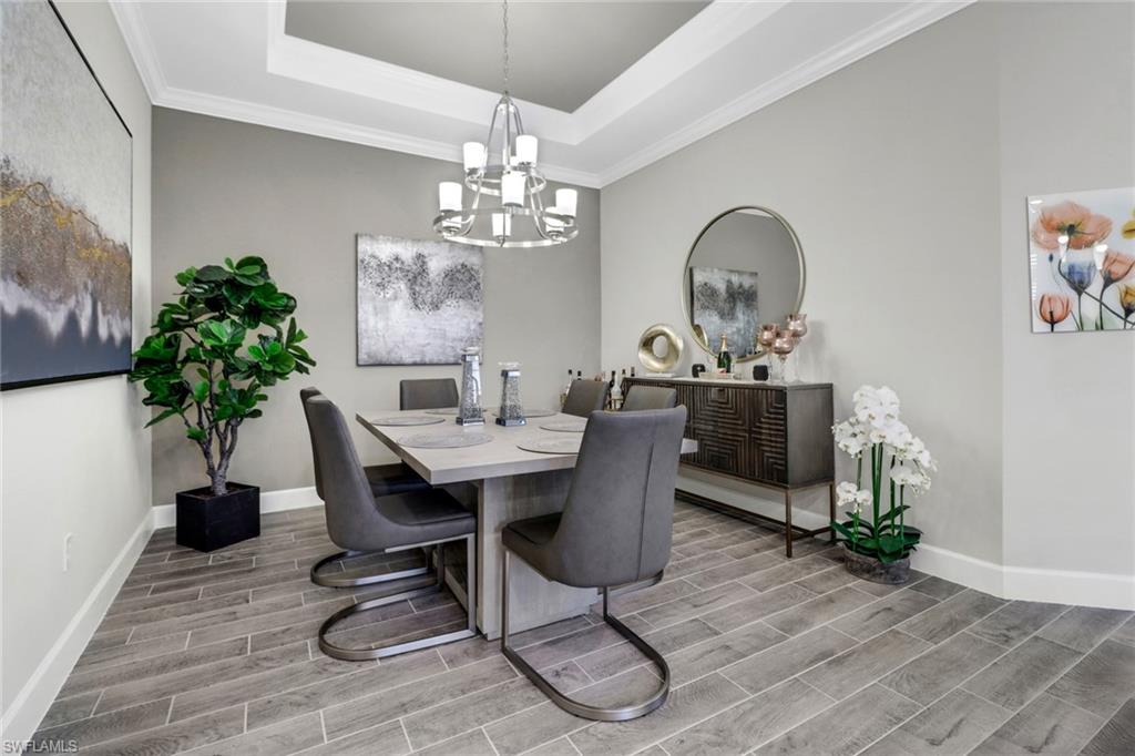 Dining space featuring wood tiled floors, suspended lighting, crown molding, and a raised ceiling