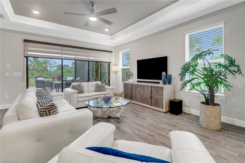 Living area featuring wood finish floors, a ceiling fan, a tray ceiling, crown molding, and recessed lighting