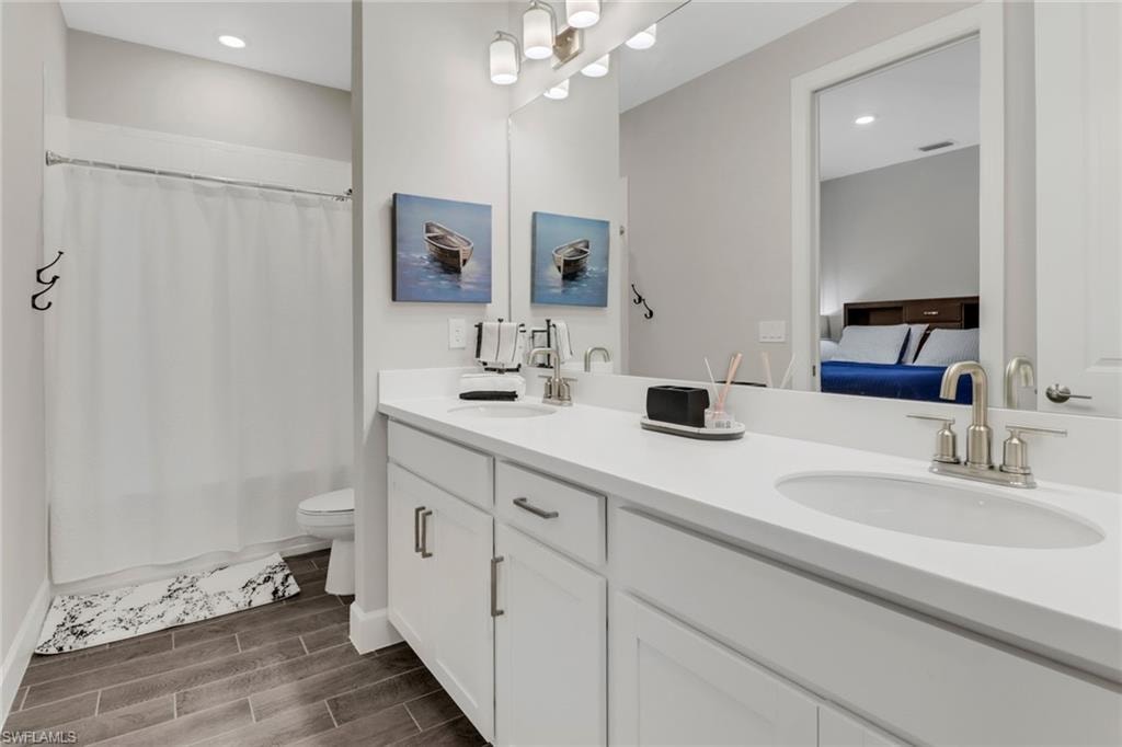 Full bathroom with double vanity, wood finish floors, ensuite bath, recessed lighting, and shower / tub combo with curtain