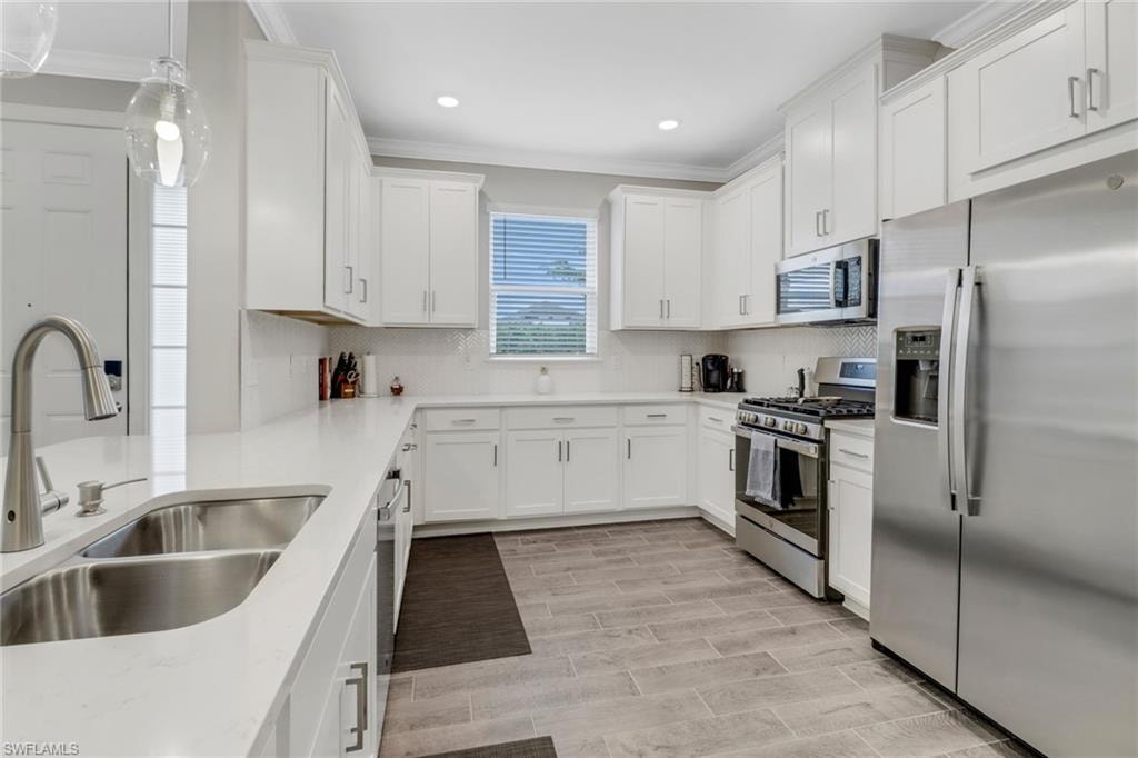 Kitchen with stainless steel appliances, white cabinets, ornamental molding, pendant lighting, and light stone counters